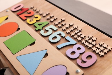 Busy board with colorful numbers and shapes on light background, closeup. Baby sensory toy