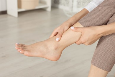 Woman rubbing sore leg at home, closeup
