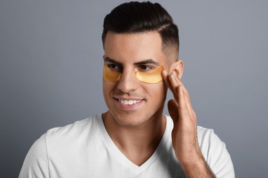 Man applying golden under eye patch on grey background