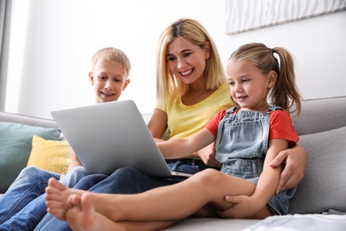 Happy mother using laptop with her children on sofa at home
