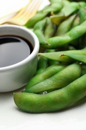 Photo of Green edamame beans in pods served with soy sauce on plate, closeup