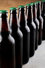 Photo of Many bottles of beer on grey table against light brown background, closeup