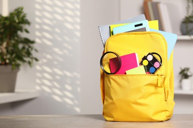 Yellow backpack with different school stationery on table indoors, space for text