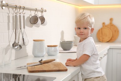 Curious little boy near kitchen counter with cutting board and sharp knife
