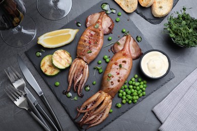 Photo of Tasty grilled squids served on black table, flat lay
