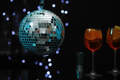 Shiny disco ball hanging over bar counter with cocktails in nightclub, space for text