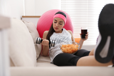 Lazy young woman with sport equipment and junk food at home