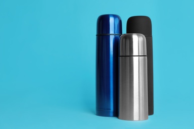 Stylish thermo bottles on light blue background, space for text