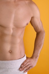 Shirtless man with slim body and towel wrapped around his hips on yellow background, closeup