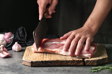 Man cutting fresh raw meat on table against dark background, closeup