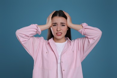 Young woman suffering from headache on blue background. Cold symptoms