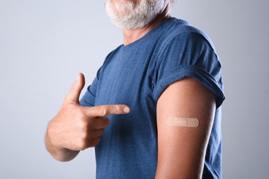Senior man pointing at arm with bandage after vaccination on grey background, closeup
