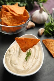 Photo of Delicious hummus with nacho chip and parsley on black table, closeup