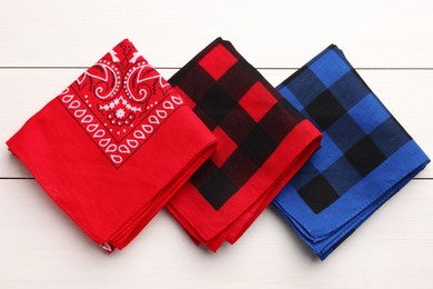 Folded bandanas with different patterns on white wooden table, flat lay