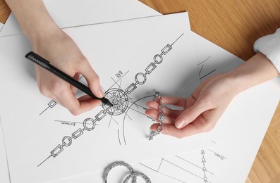 Photo of Jeweler drawing sketch of elegant bracelet on paper at wooden table, top view