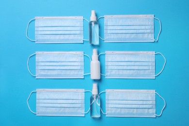 Hand sanitizers and medical masks on light blue background, flat lay