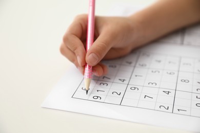 Little child solving sudoku puzzle at white table, closeup