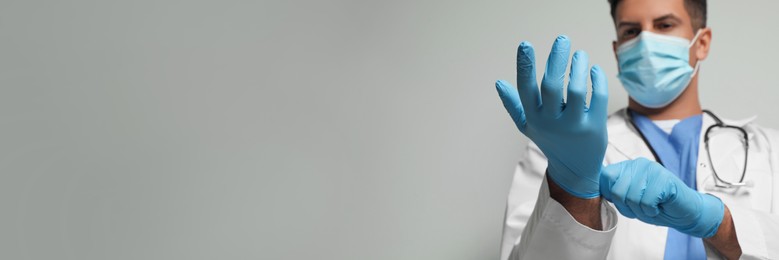Image of Surgeon putting on medical gloves against light grey background, focus on hands. Banner design with space for text