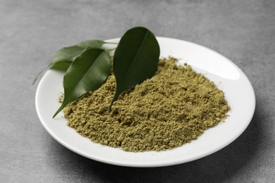 Photo of Henna powder and green leaves on grey background. Natural hair coloring