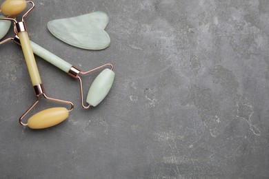 Gua sha stone and different face rollers on grey table, flat lay. Space for text