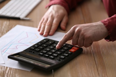 Man using calculator at wooden table, closeup