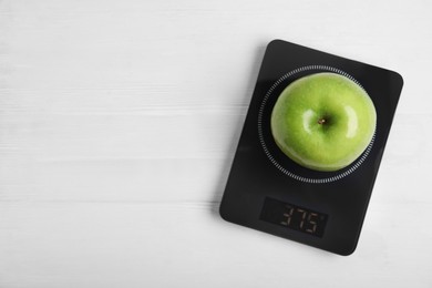 Ripe green apple and electronic scales on white wooden table, top view. Space for text