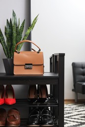 Shelving unit with stylish shoes and bag near grey wall in hallway