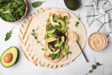Photo of Tortilla with hummus and vegetables on white table, flat lay