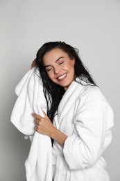 Beautiful young woman in bathrobe drying hair with towel on light background