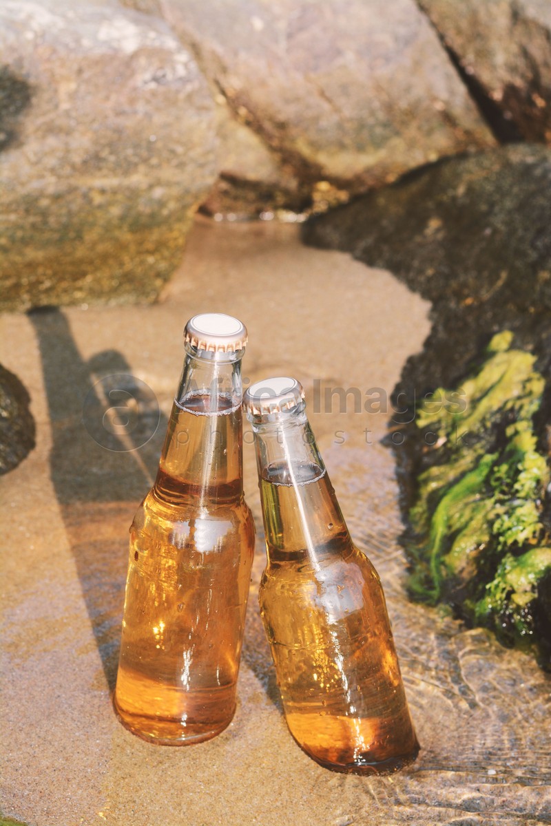 Bottles of cold beer near rock on sandy beach
