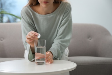 Woman putting medicine for hangover into glass of water at home, closeup