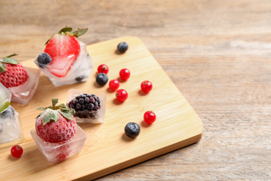 Ice cubes with different berries and mint on wooden table
