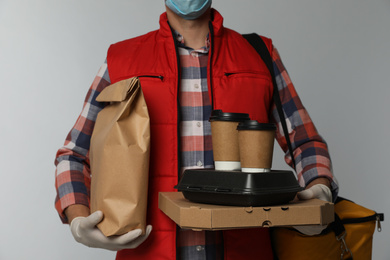 Courier in protective gloves holding order on light background, closeup. Food delivery service during coronavirus quarantine