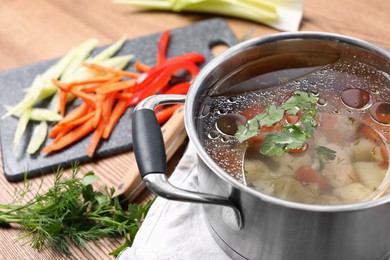 Pot of delicious vegetable bouillon and ingredients on wooden table, closeup