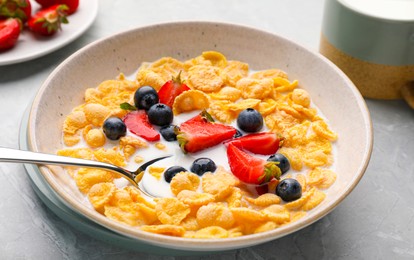 Bowl of tasty crispy corn flakes with milk and berries on light grey table, closeup