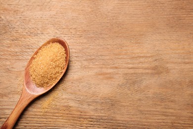 Spoon with brown sugar on wooden table, top view. Space for text
