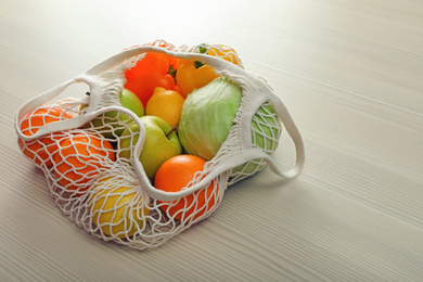 Net bag with vegetables and fruits on wooden table
