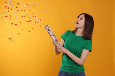 Photo of Happy teenage girl blowing up party popper on orange background