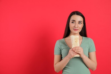 Photo of Dreamy young woman holding tasty shawarma on red background. Space for text