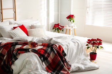 Photo of Christmas bedroom interior with red woolen blanket and poinsettias