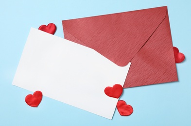 Blank card, envelope and decorative hearts on light blue background, flat lay with space for text. Valentine's Day celebration