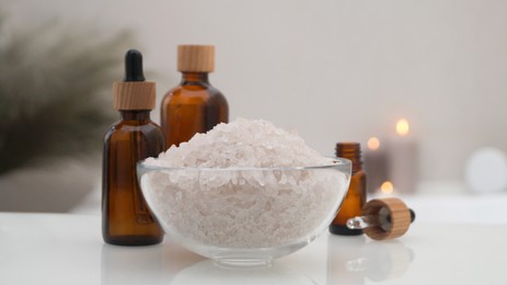 Glass bowl with bath salt and cosmetic products on white countertop indoors, closeup