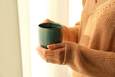 Woman holding elegant cup with tea near window indoors, closeup