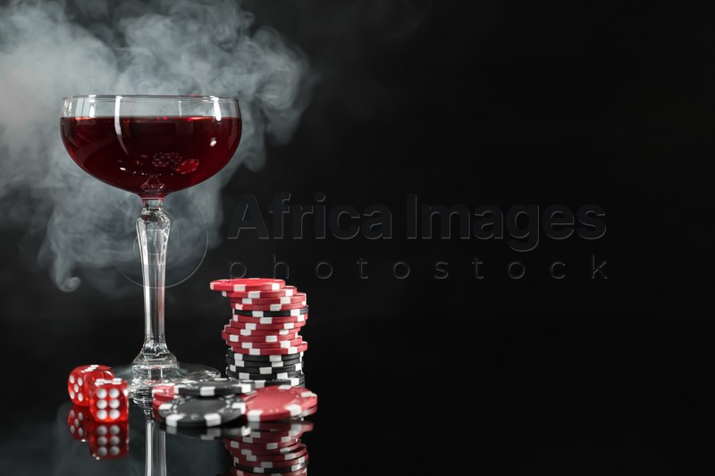 Casino chips, dice and glass of wine on dark background with smoke. Space for text
