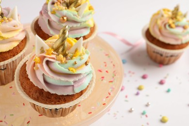 Photo of Dessert stand with cute sweet unicorn cupcakes on white table, closeup. Space for text