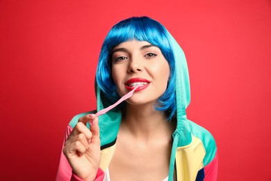 Fashionable young woman in colorful wig chewing bubblegum on red background