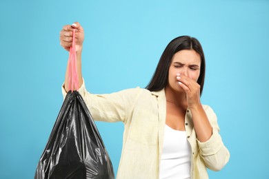 Woman holding full garbage bag on light blue background
