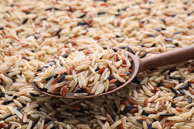 Mix of different brown rice and wooden spoon, closeup