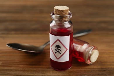 Vials of poison with spoon on wooden table, closeup