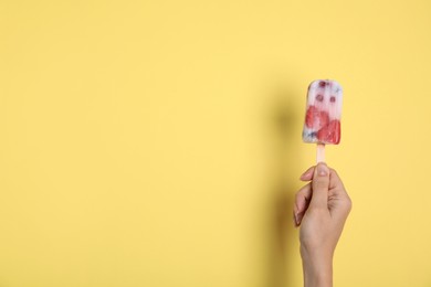 Woman holding berry popsicle on yellow background, closeup. Space for text